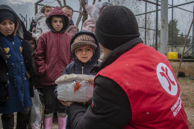 HCI Aid Worker hands out a parcel to a small girl.